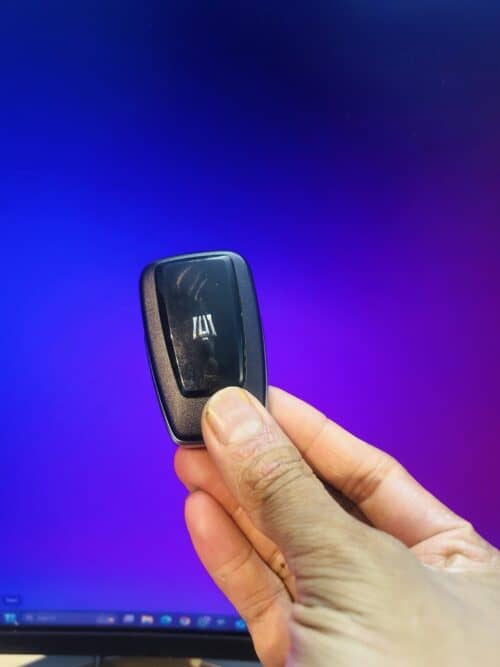 Compact remote control device held in hand against a vibrant purple background.