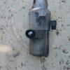 Close-up of a used automotive fuel pump lying on sandy ground, showing signs of wear and dirt.