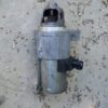 Automotive starter motor lying on gravel, used in vehicle repair and maintenance.