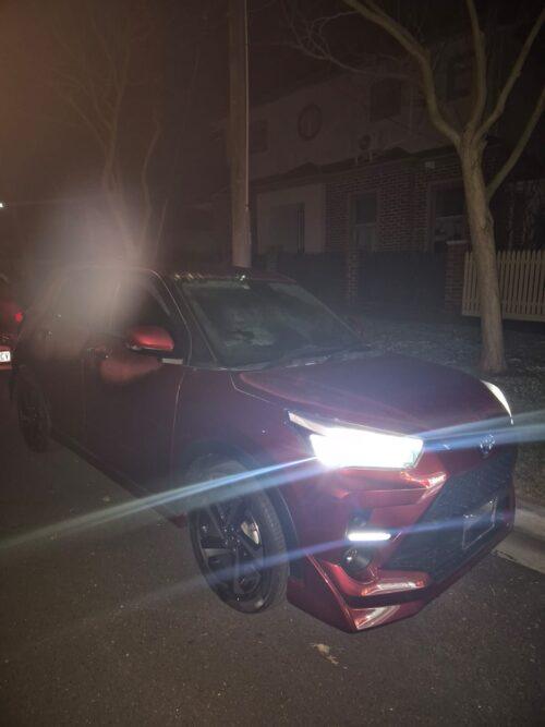 Red sedan car parked on street at night with headlights on.