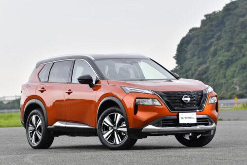 Nissan X-Trail SUV on open road with green landscape in background.