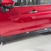 Red car door with side mirror and handle, close-up view.