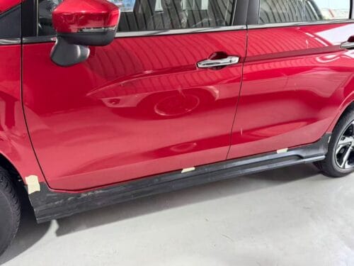 Red car door with side mirror and handle, close-up view.