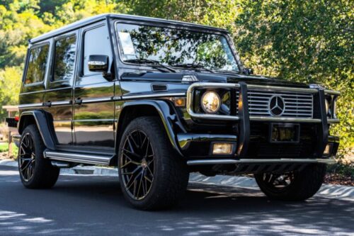 Black Mercedes-Benz G-Class SUV parked on a scenic street with trees in the background.