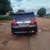 Black Toyota minivan parked on dirt road in rural setting with trees and open sky.