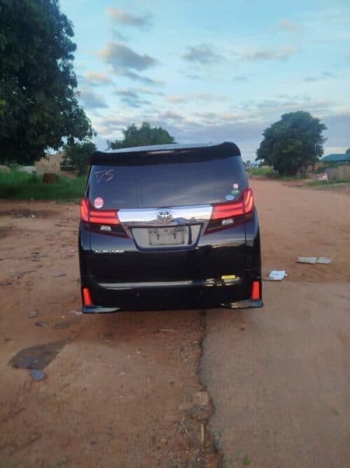 Black Toyota minivan parked on dirt road in rural setting with trees and open sky.